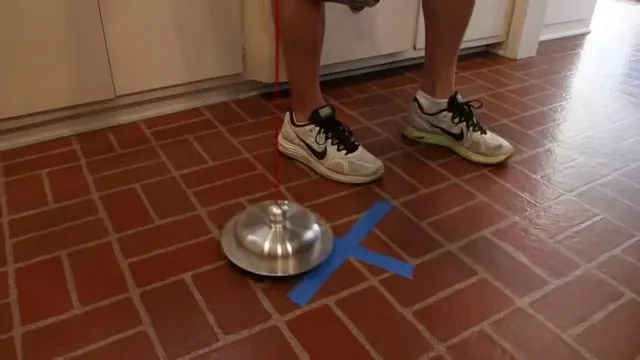 Round metal listening device on a red tile floor marked with blue tape, with a person standing beside it