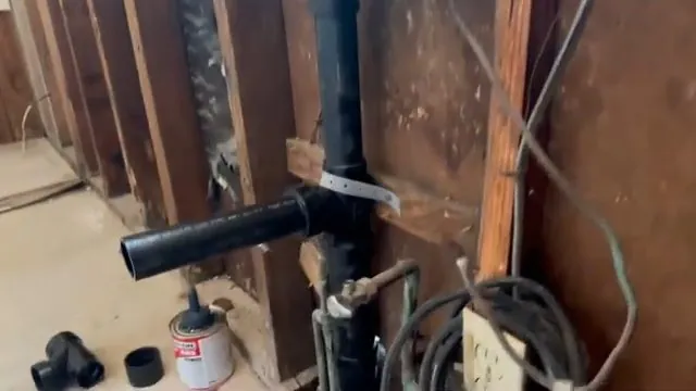 Black drain pipe fittings exposed inside an open wall with wood studs