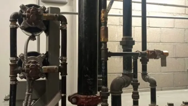 Black iron pipes with valves and fittings running along a concrete block wall