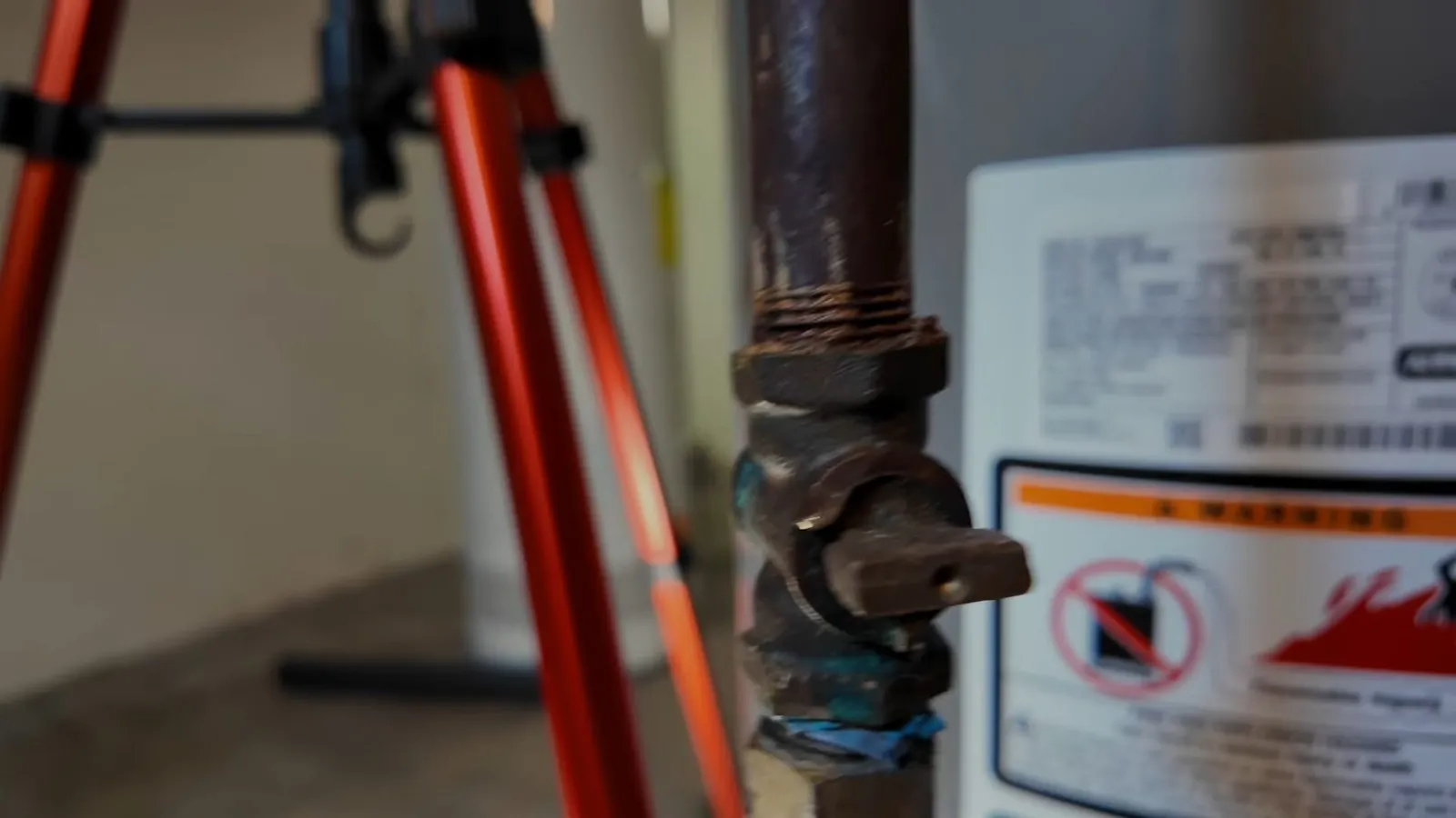 Black iron gas pipe and shutoff valve beside a water heater with a warning label