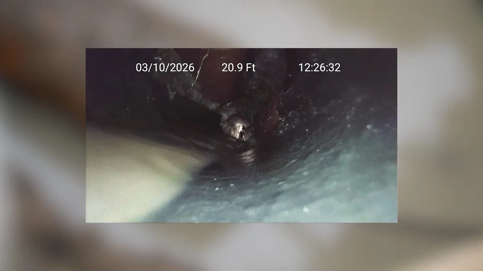 Drain camera view inside a pipe with date and footage readout overlaid