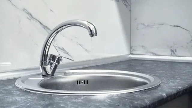 Chrome faucet over a round stainless sink with water dripping from the spout