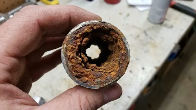 Hand holding a cut section of galvanized pipe with the inside heavily rusted and narrowed