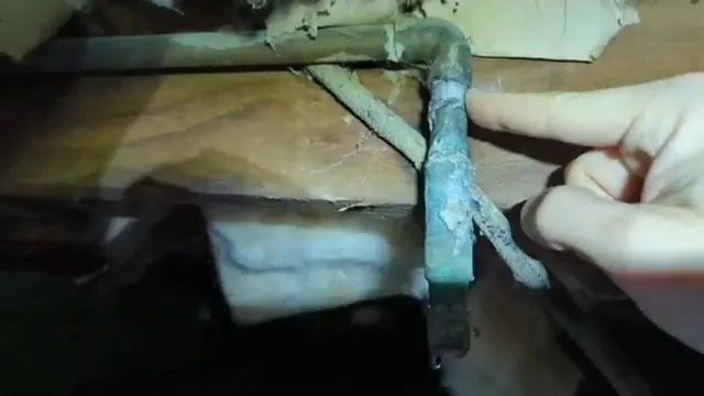 Finger pointing at a green corroded copper elbow in a crawlspace