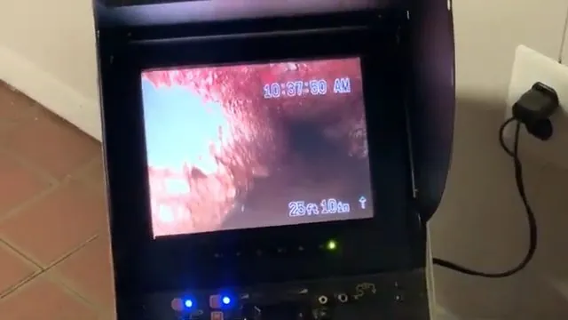 Drain camera monitor on a stand showing the inside of a pipe with a depth reading