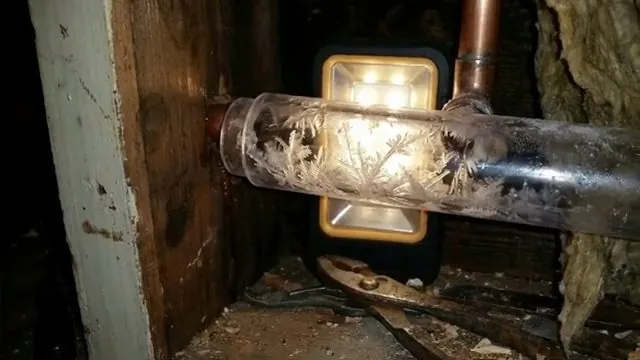 Frost crystals inside a clear pipe section lit by a work light in a framed cavity