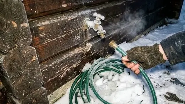 Frosted outdoor hose bib on a wood wall with a green hose coiled on snow below