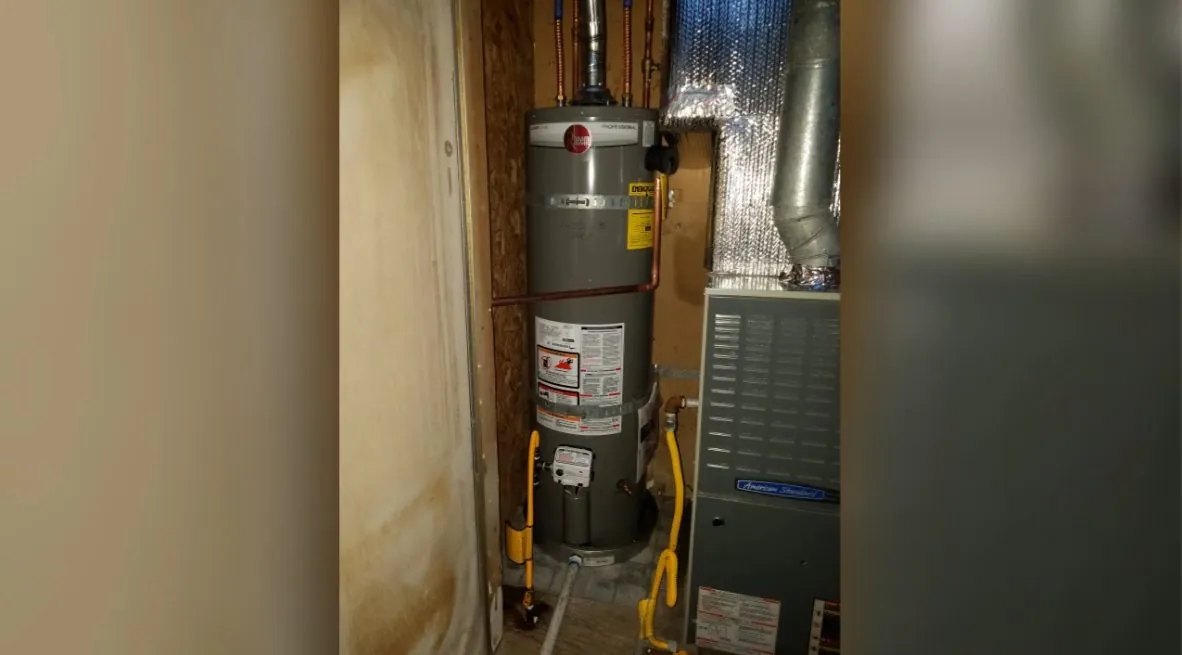 Gas water heater in a narrow utility closet beside a furnace with a vent pipe overhead