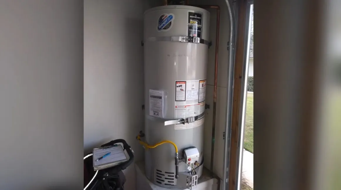 Gas water heater in a utility area with its gas supply line and a small monitor on the floor