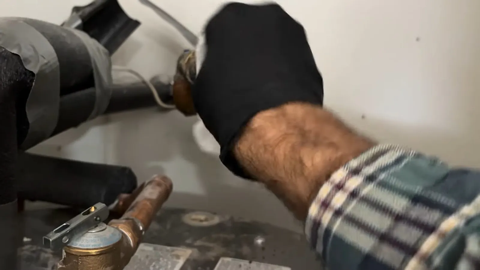 Black gloved hand reaching to a valve and copper lines above a water heater tank