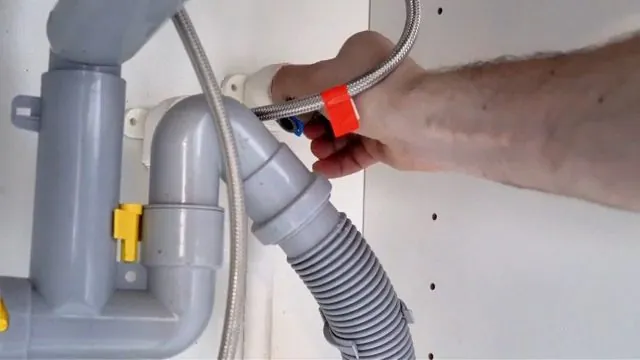 Gray plastic drain trap and braided supply line under a sink with a hand holding the line
