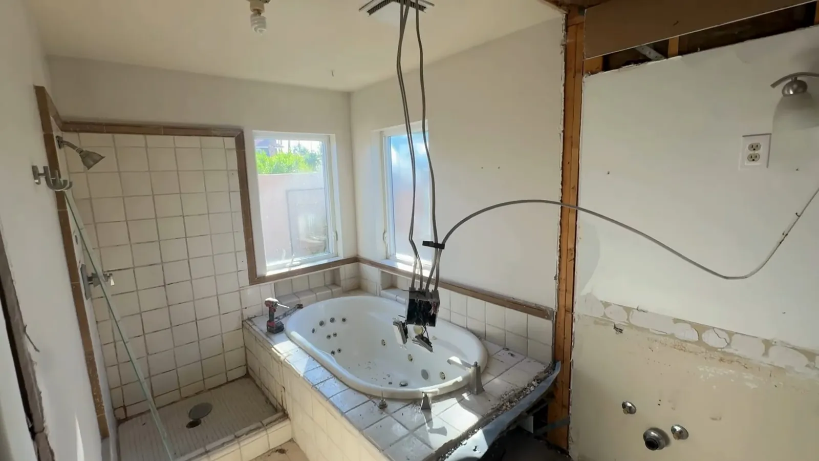 Gutted bathroom with a tiled shower, a jetted tub and bare wall studs