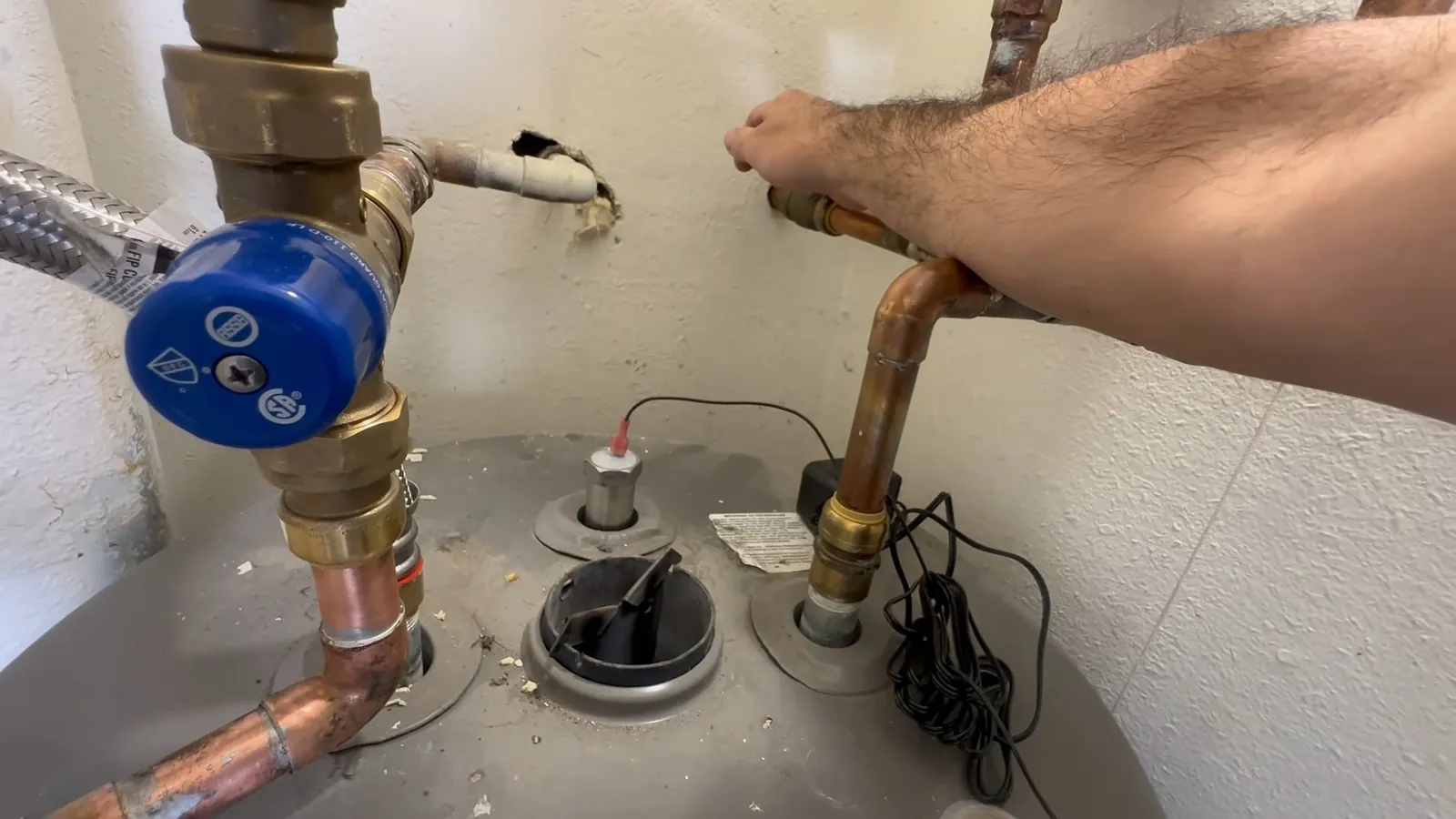 Arm reaching to a copper line and blue valve above the top of a water heater