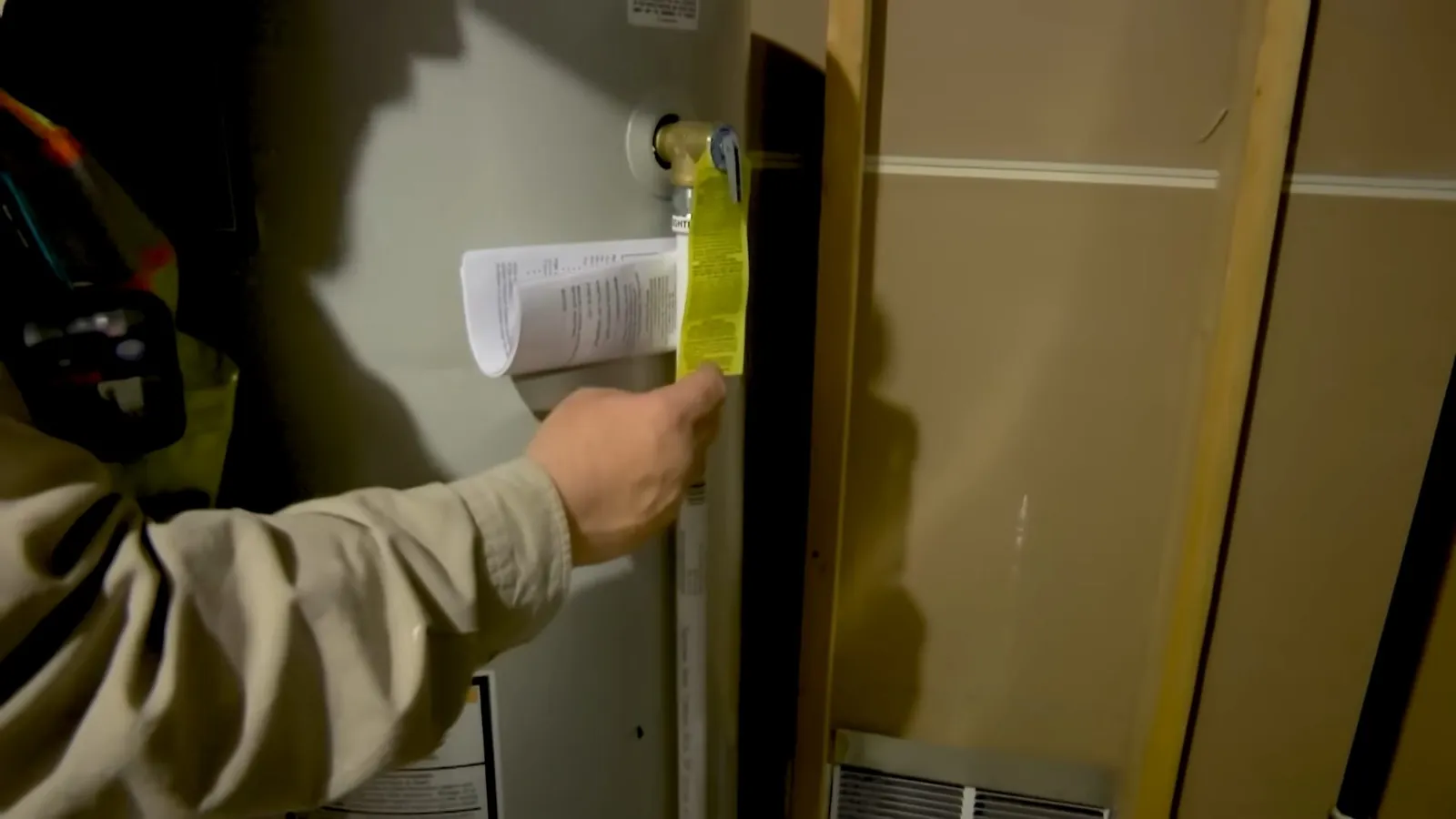 Hand holding a yellow tag on a pipe beside a wall with papers tucked behind it