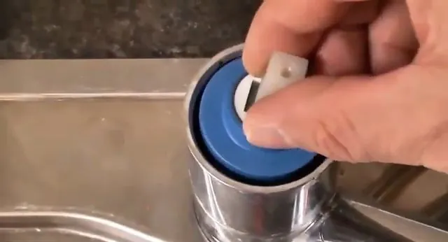 Hand fitting a blue plastic cartridge into the body of a faucet at a stainless sink