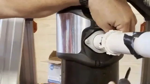 Hands tightening a white drain pipe at the side of a stainless garbage disposal