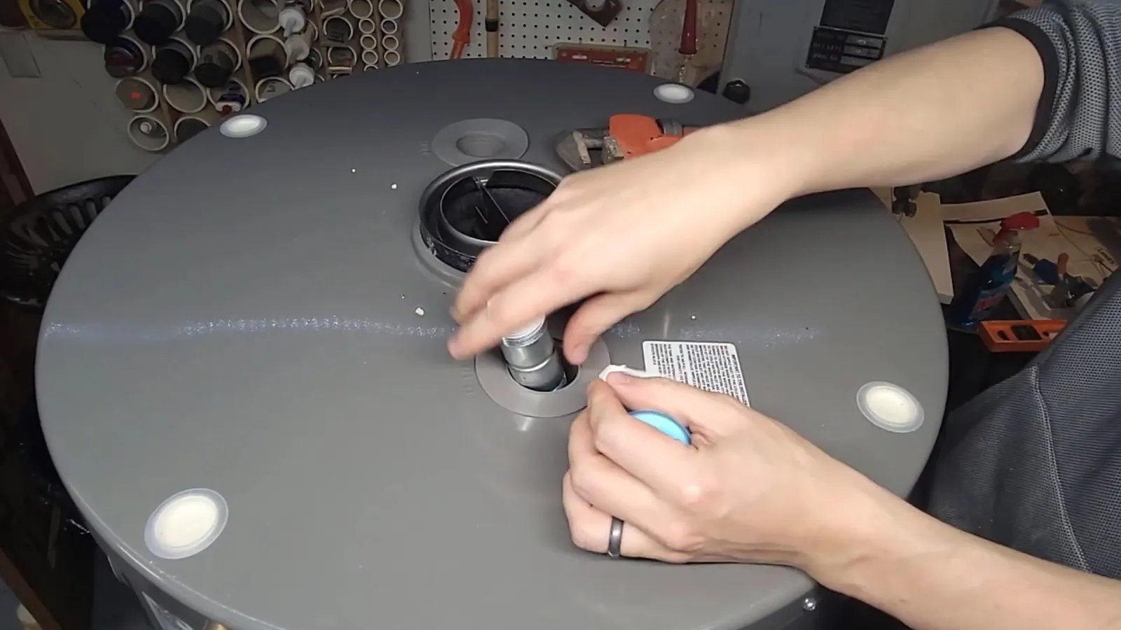 Hands working on the inlet and outlet fittings on top of a gray tank water heater