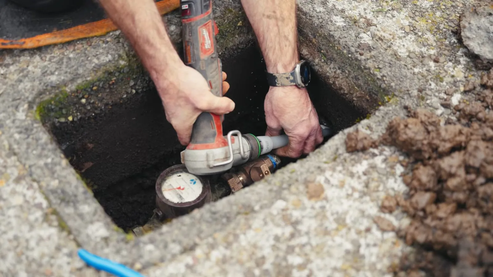 Hands using a tool at a water meter inside a concrete ground box