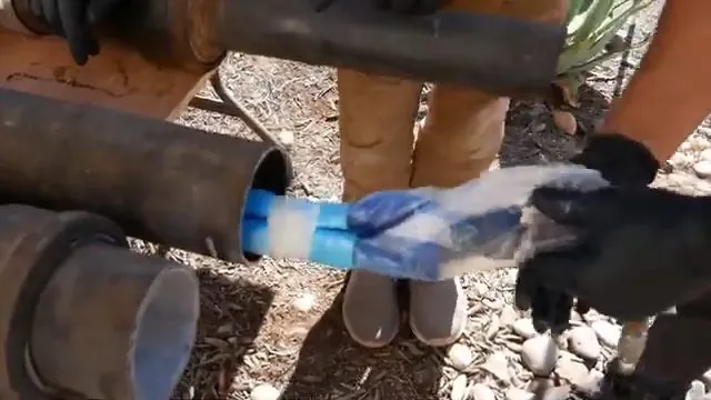 Gloved hands feeding a blue sleeve liner into the end of a black pipe