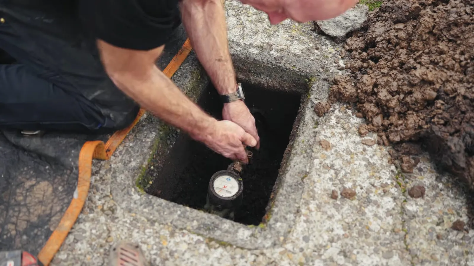 Man kneeling at an in-ground water meter box and reading the meter dial