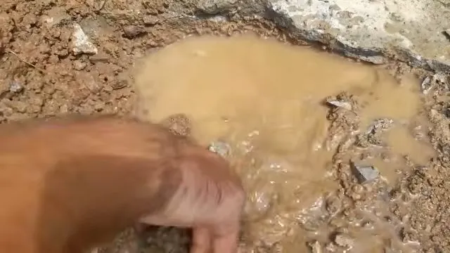 Hand reaching toward a pool of muddy water standing in gravel and dirt