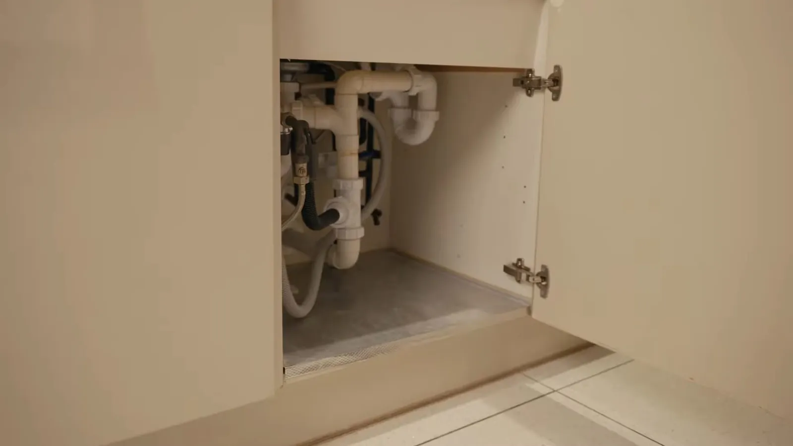 Open vanity cabinet showing white drain pipes and supply lines inside