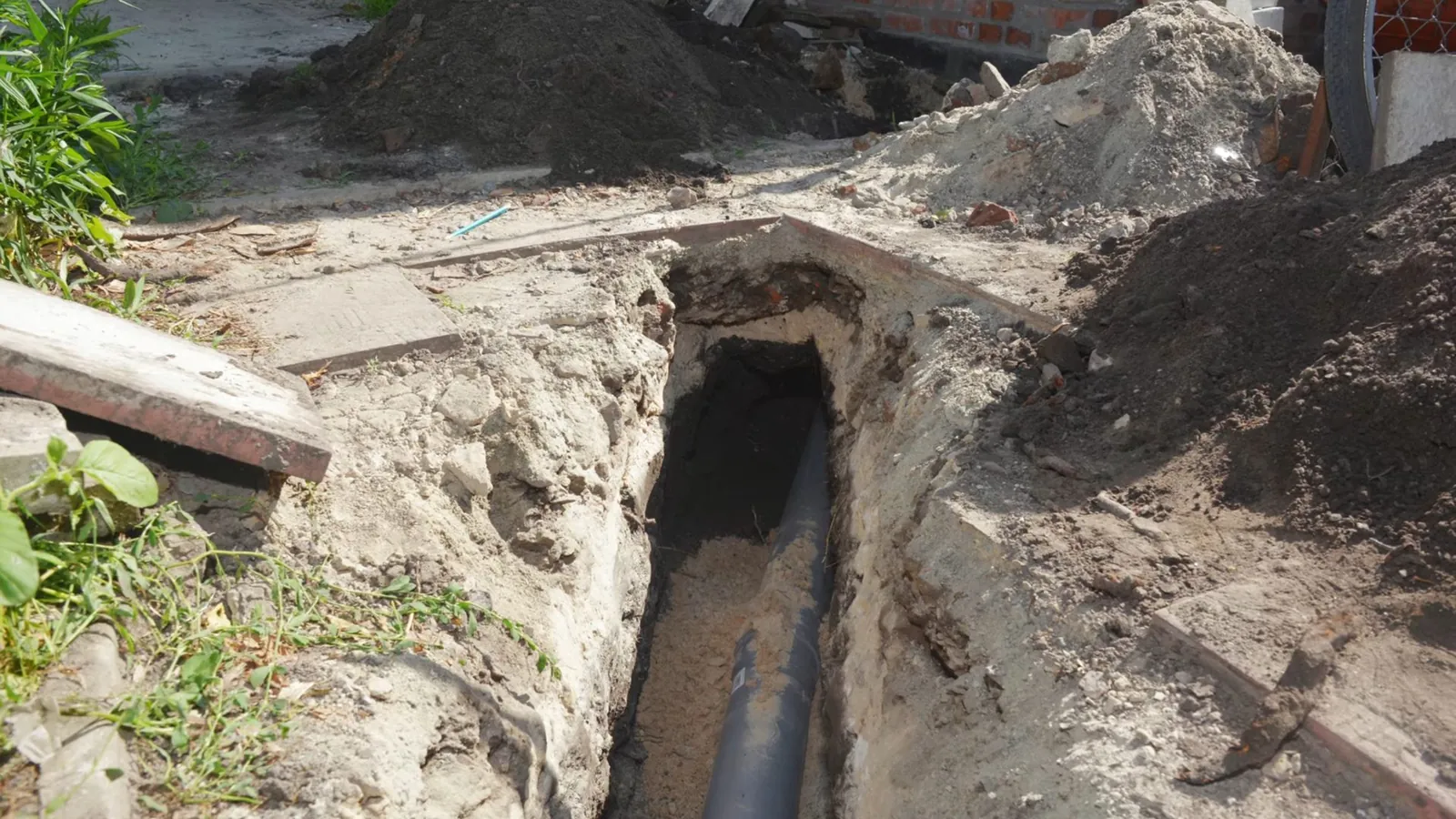Long open trench in a yard with a dark sewer pipe at the bottom and soil piled beside it