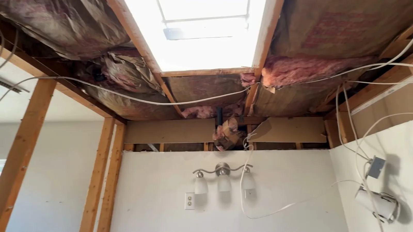 Opened ceiling above a bathroom wall showing joists, pink insulation and wiring