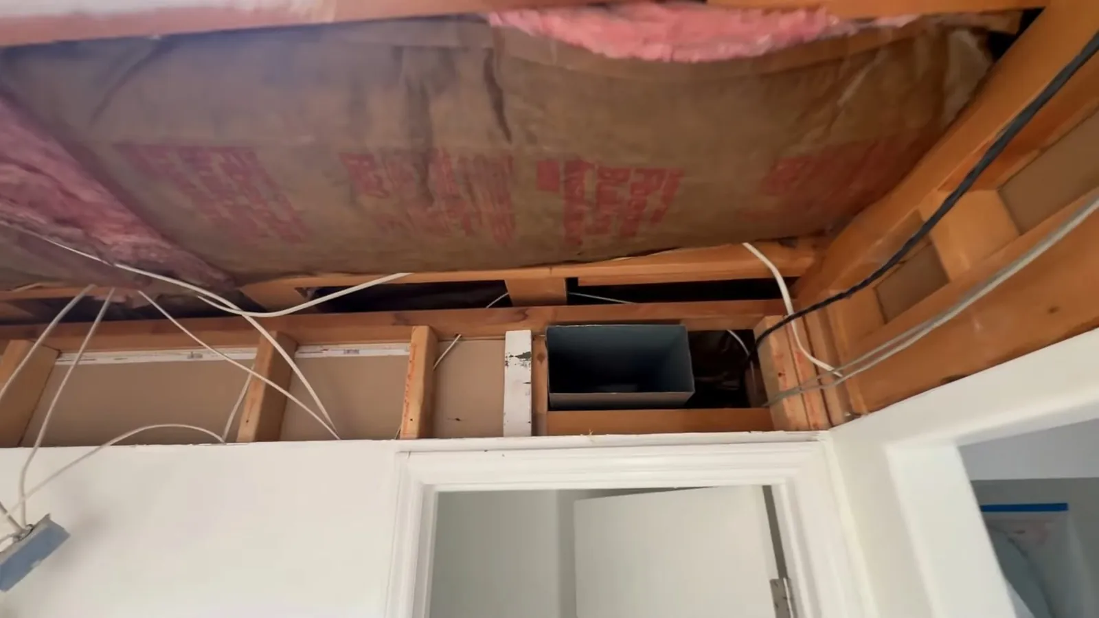 Opened ceiling showing wood joists and pink insulation above a doorway