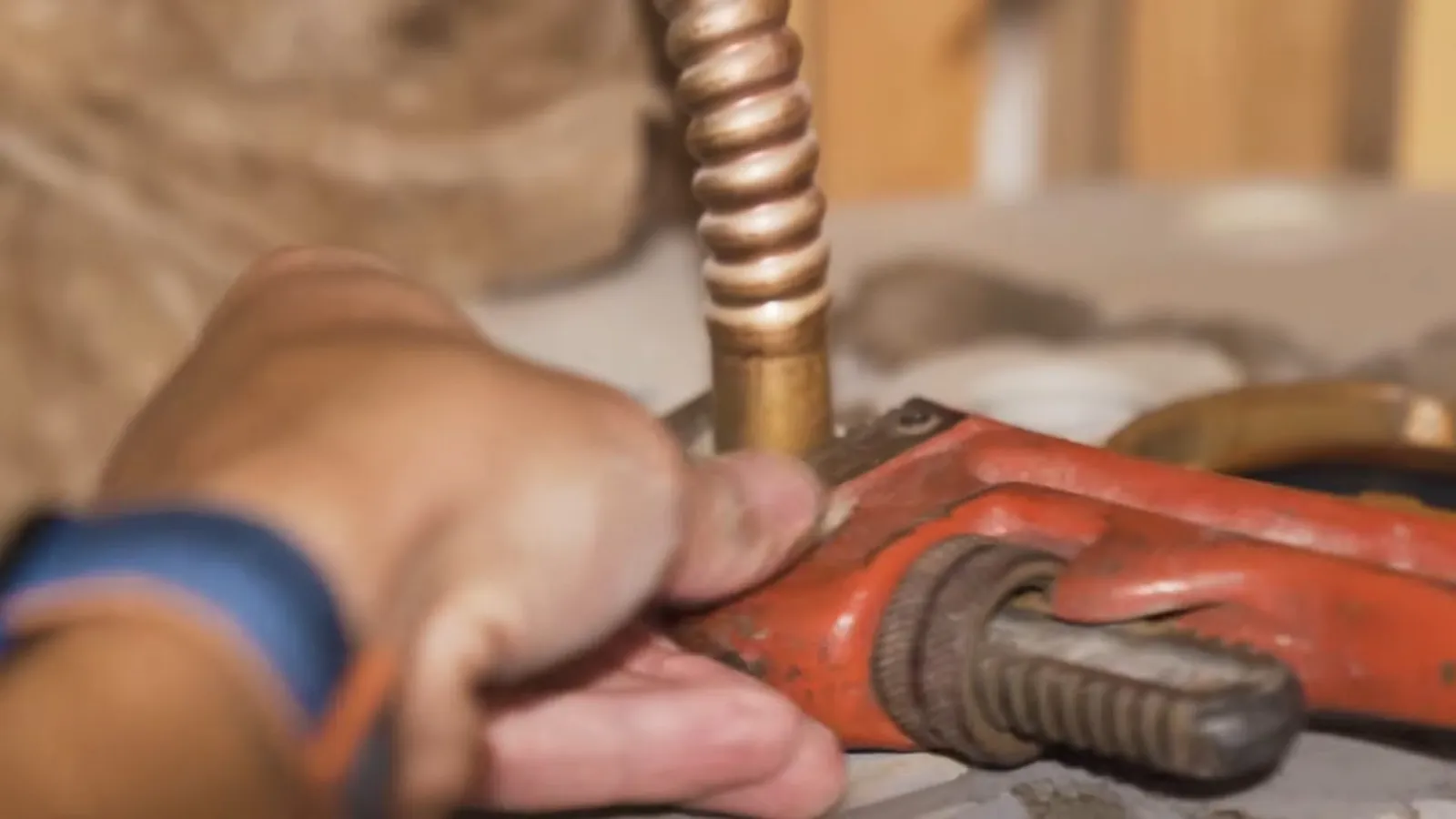 Hand with a pipe wrench on a flexible copper line at the top of a water heater