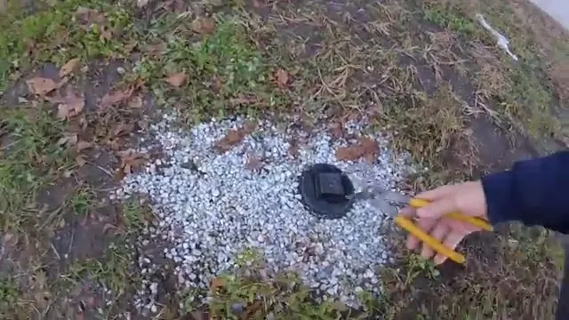 Hand with yellow pliers at a black cleanout cap set in a patch of white gravel