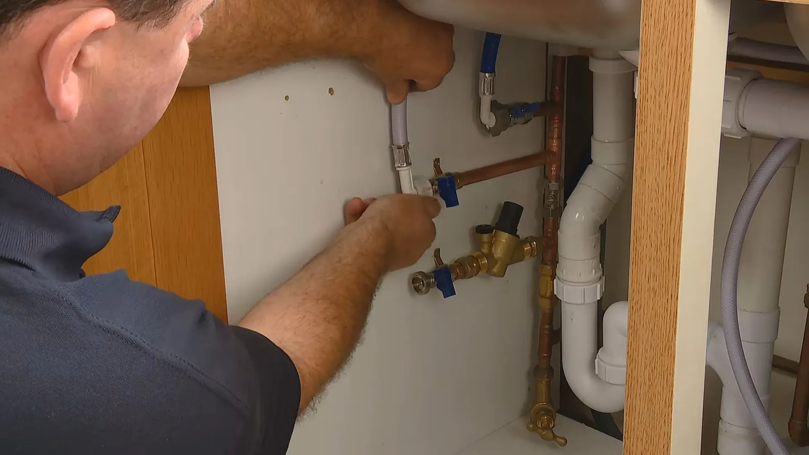 Man reaching into a vanity cabinet to work on copper supply pipes and shutoff valves