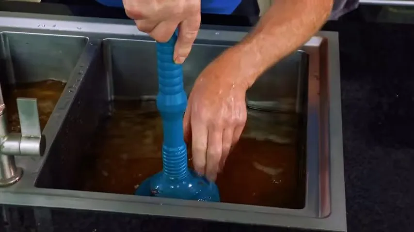 Hands working a blue plunger in a sink full of dirty standing water