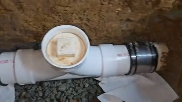 White PVC cleanout tee with a screw cap lying in dirt