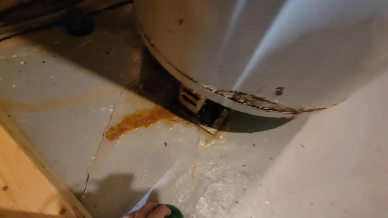 Rust-colored stain on a basement floor around the base of a water heater tank