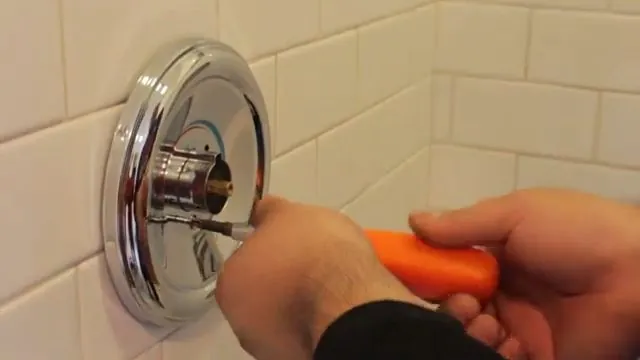 Hand using a screwdriver on a chrome shower valve trim plate on a tiled wall