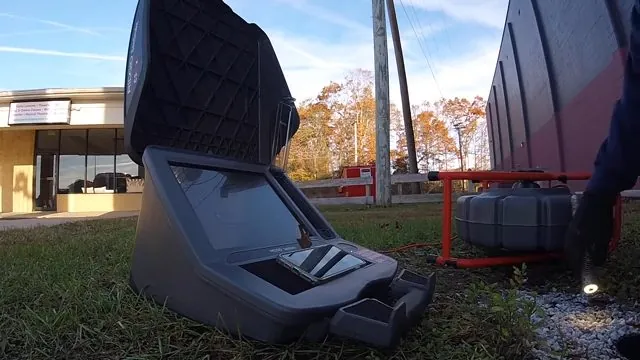 Sewer inspection camera case open on grass beside a red cable reel in front of a building