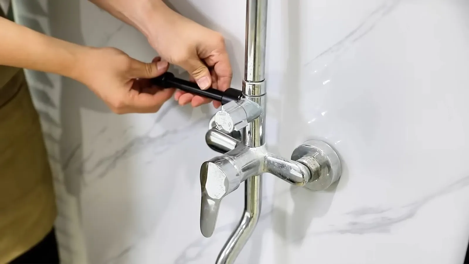 Hands holding a tool at a chrome shower faucet valve on a white marble wall
