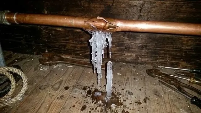 Copper pipe with a split seam and icicles hanging below it over a dirt floor