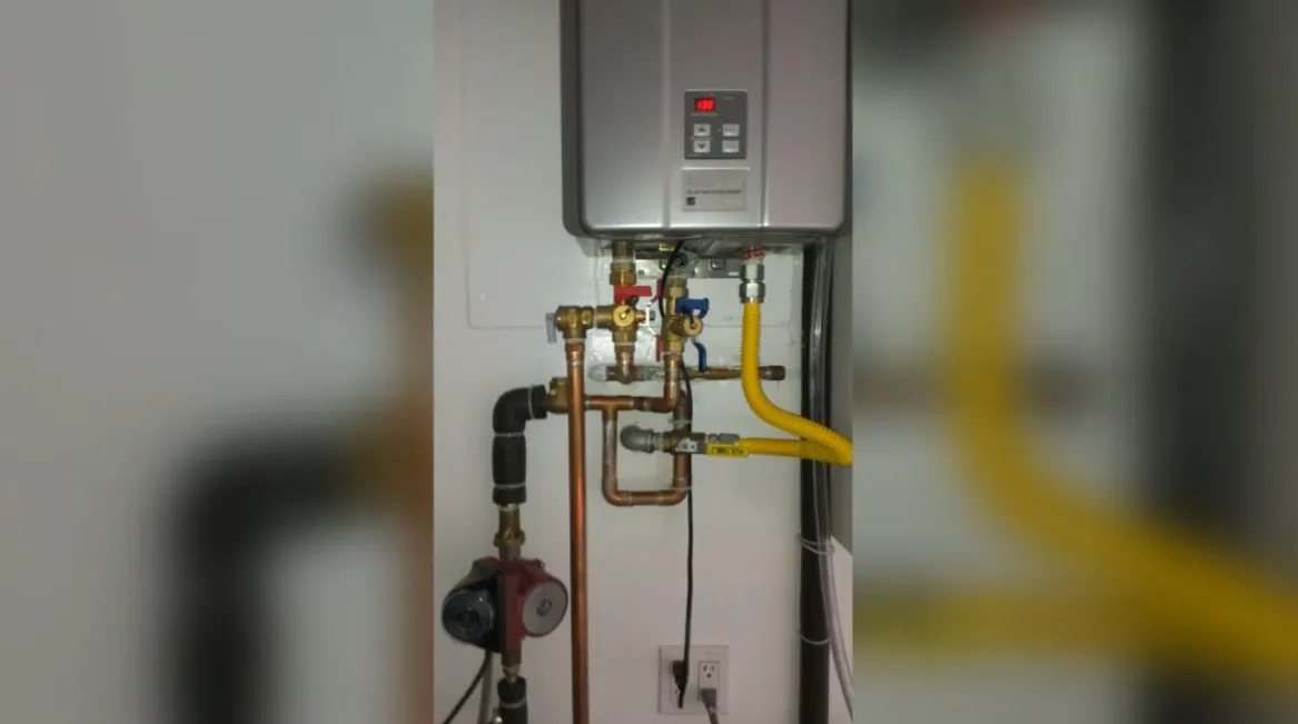 Wall-mounted tankless water heater indoors with copper pipes and a yellow gas line below it