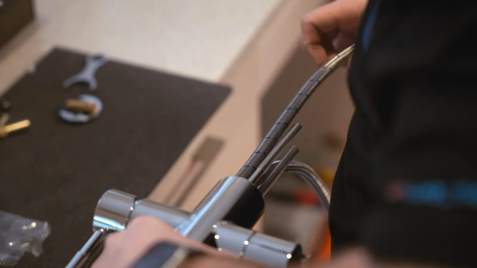 Hand holding a braided supply line under a sink with an adjustable wrench nearby