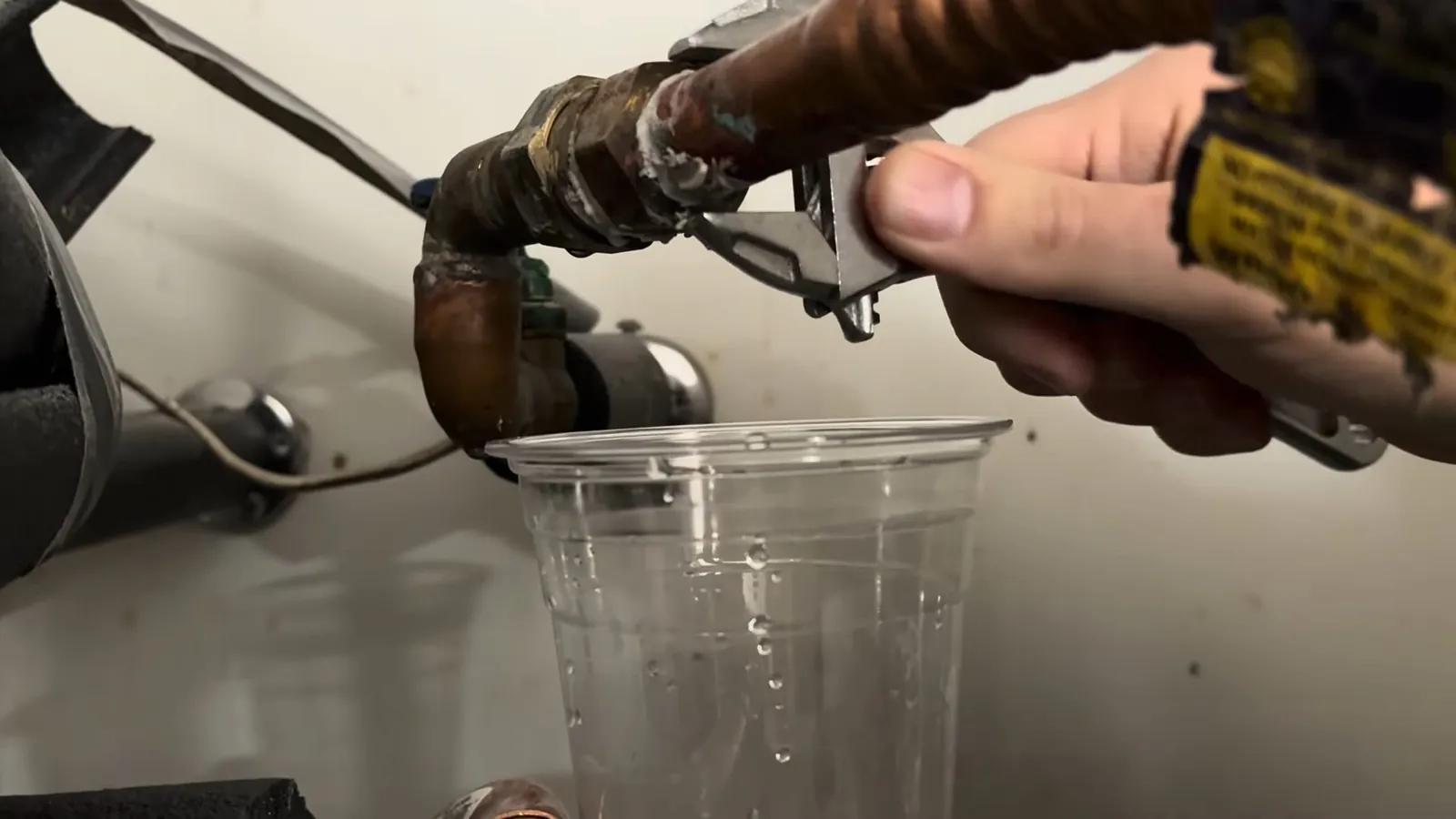 Hand opening a brass drain valve with water running into a clear plastic cup