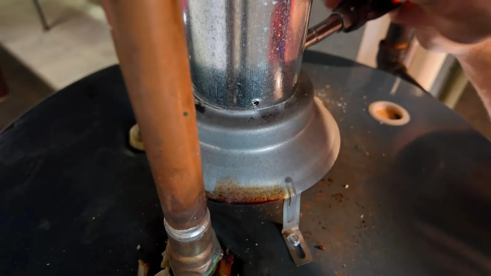 Metal flue pipe and a copper water line at the top of a dark water heater tank