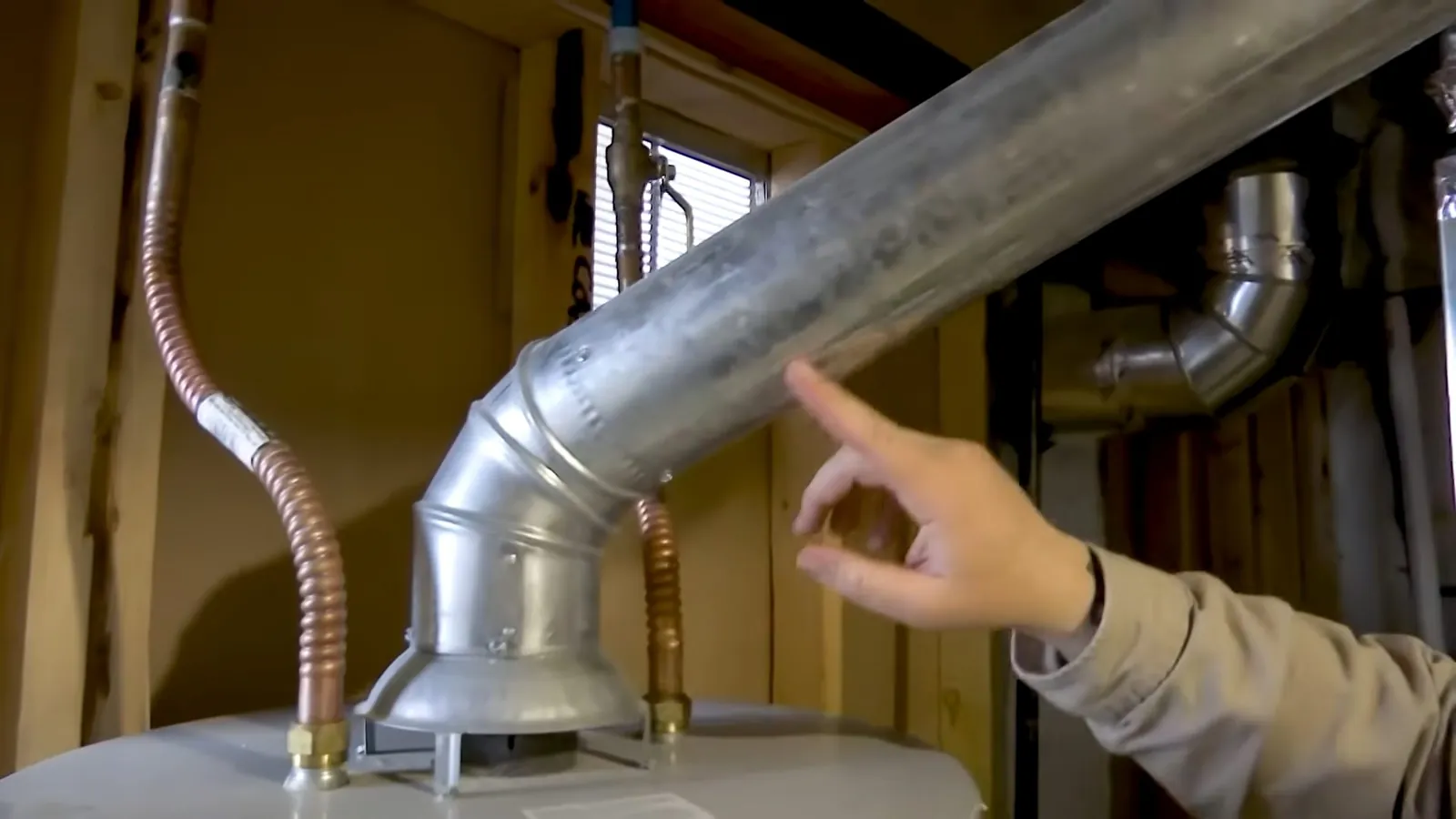 Galvanized flue pipe rising from the top of a water heater beside copper supply lines