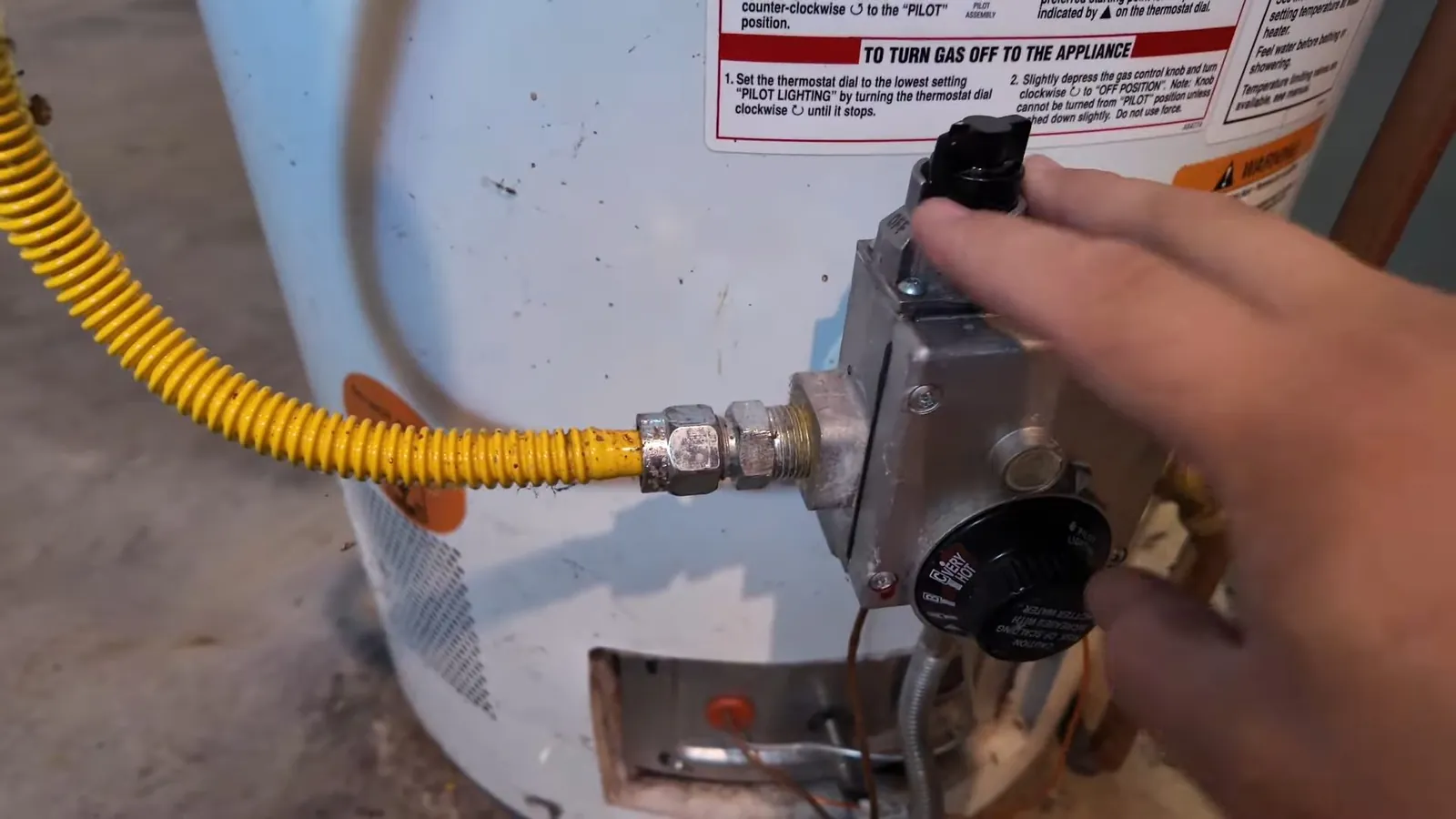 Hand at the gas control of a water heater with a yellow flexible gas line attached