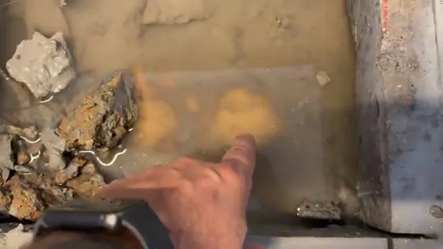 Hand pointing at shallow water pooled on a concrete surface beside broken rock